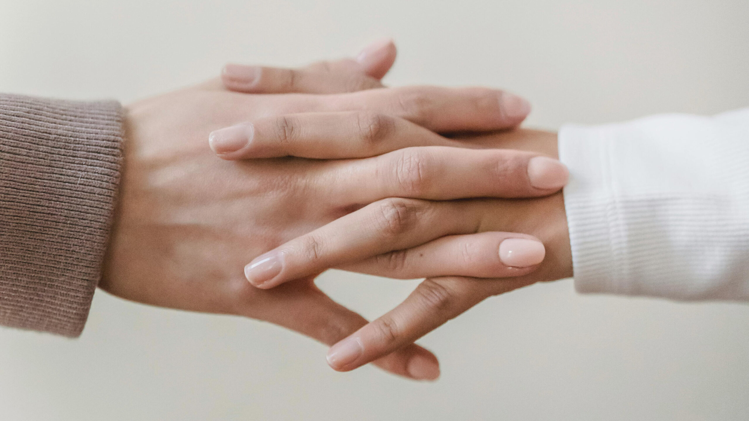 Kaksi henkilöä pitää käsiä, kasvot eivät näy, taustalla seinä.