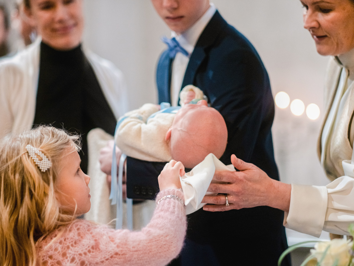 Pieni tyttö kuivaa papin kanssa kastetun vauvan päätä valkoisella liinalla.