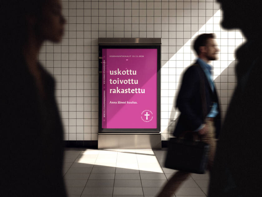 Kaupunkitilan seinällä oleva digitaalinen mainostaulu, jossa violetti juliste. Julisteessa teksti: ‘uskottu, toivottu, rakastettu – anna äänesi kuulua’. Etualalla ohikulkijoita liikkeessä.