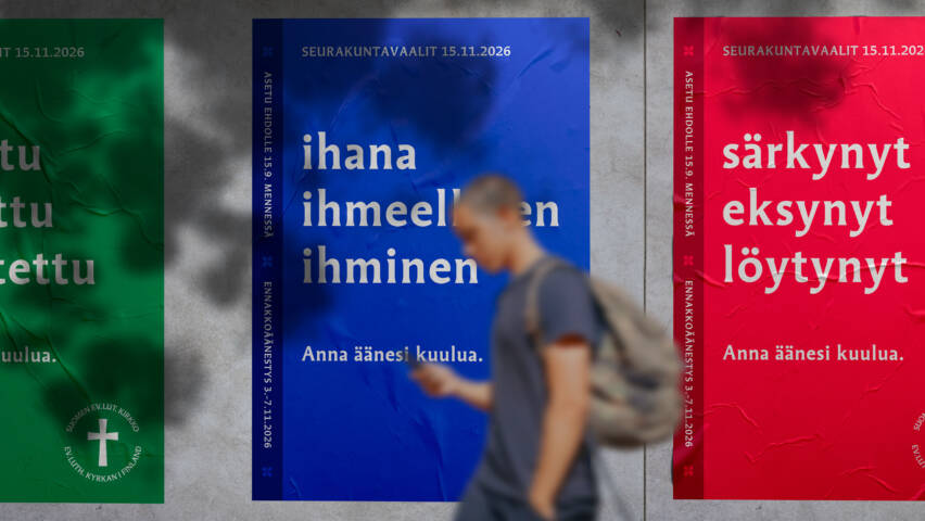 Kaupunkiseinällä kolme värikästä julistetta seurakuntavaaleista. Keskimmäisessä sinisessä julisteessa teksti: ‘ihana, ihmeellinen ihminen – anna äänesi kuulua’. Etualalla ohikulkija kävelee julisteiden ohi.