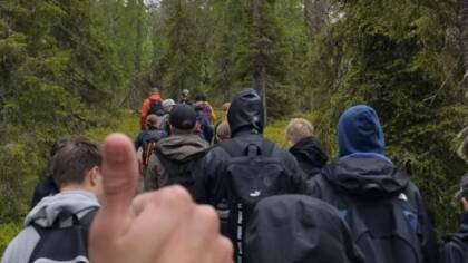 Ryhmä ihmisiä kävelee metsäpolkua pitkin. Etualalla näkyy peukku pystyssä -ele.