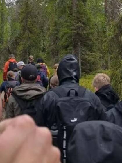 Ryhmä ihmisiä kävelee metsäpolkua pitkin. Etualalla näkyy peukku pystyssä -ele.