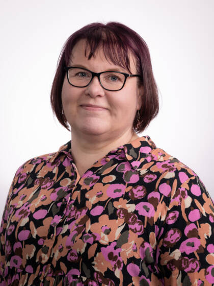 Silmälasipäinen nainen, jolla tummanpunaiset hiukset ja kukallinen kauluspaita.