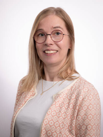 Silmälasipäinen nainen, jolla vaaleat hiukset ja vaalea kuviollinen neuletakki.