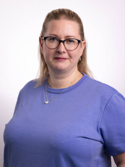 Silmälasipäinen nainen, jolla kirkkaansininen paita ja vaaleat pitkät hiukset.