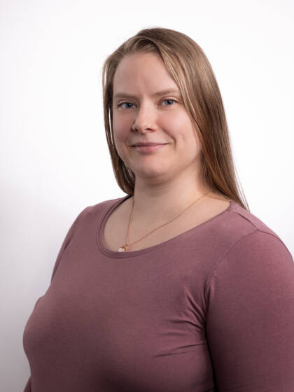 Ruskeahiuksinen hymyilevä nainen, jolla violetti paita.