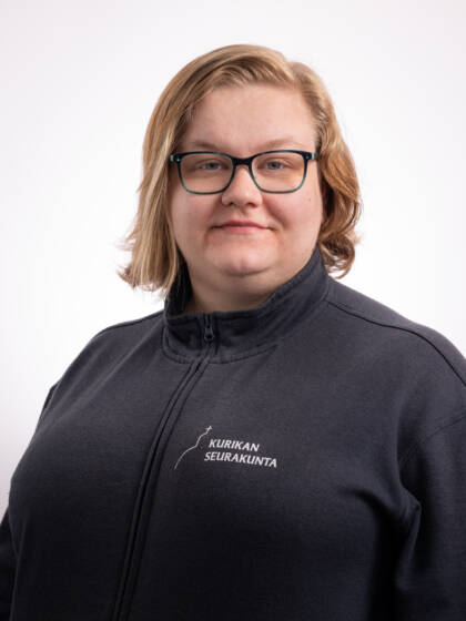 Hymyilevä vaaleahiuksinen ja silmälasipäinen nainen, jolla tummansininen paita