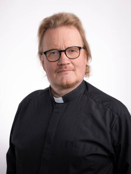 Vaaleahiuksinen silmälasipäinen miespappi, jolla musta paita