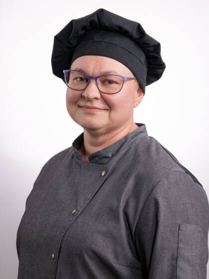 Nainen, jolla silmälasit sekä tumma kokinhattu ja -takki