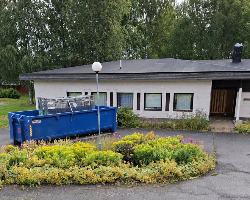Sininen roskalava rakennuksen edessä. Lavalla metallisia aitaelementtejä.