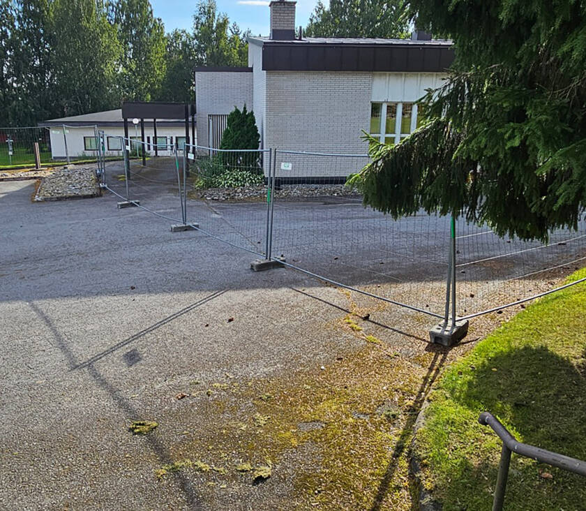 Metalliset työmaan verkkoaidat valkoisen rakennuksen edessä.