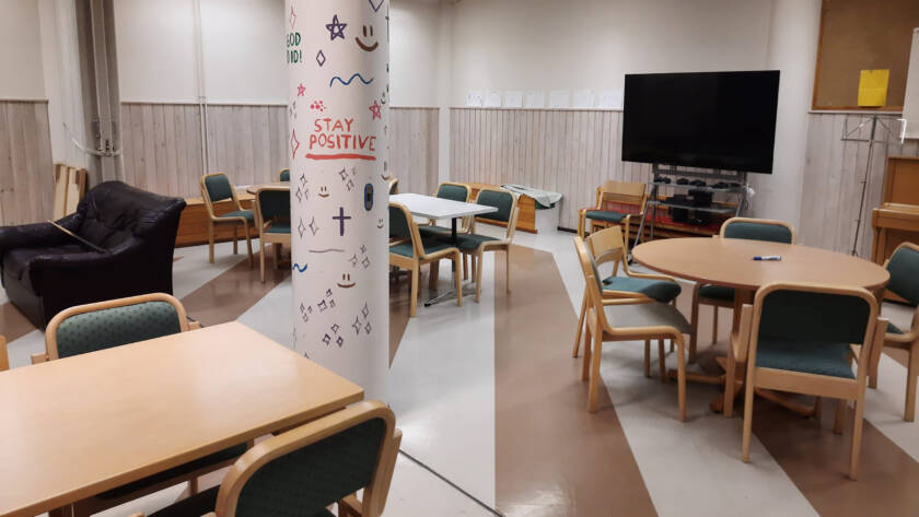 Kolme pöytää, joiden ympärillä tuoleja, taka-alalla televisio