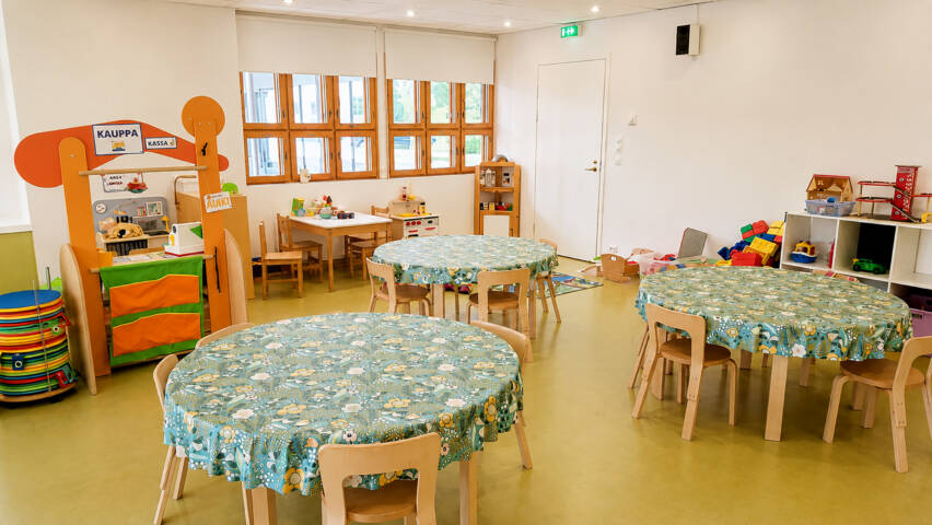 Päiväkerhotila, jossa kolme lasten pyöreää pöytää