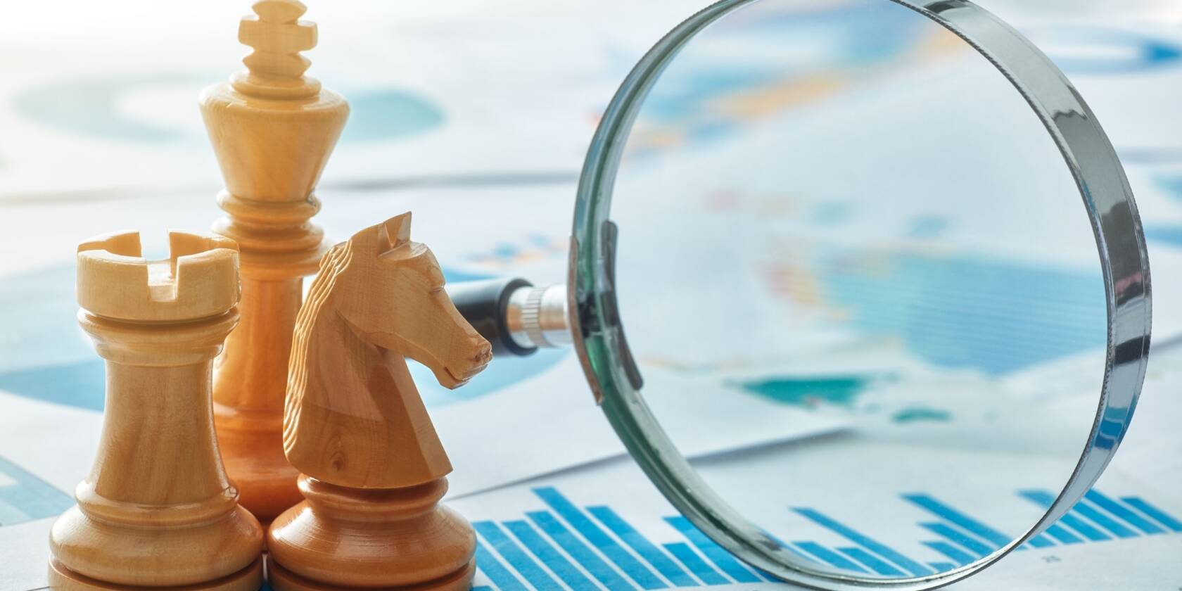 Shakkinappulat ja suurennuslasi kaavioiden päällä symboloivat strategista suunnittelua, analysointia ja tavoitteellista päätöksentekoa.