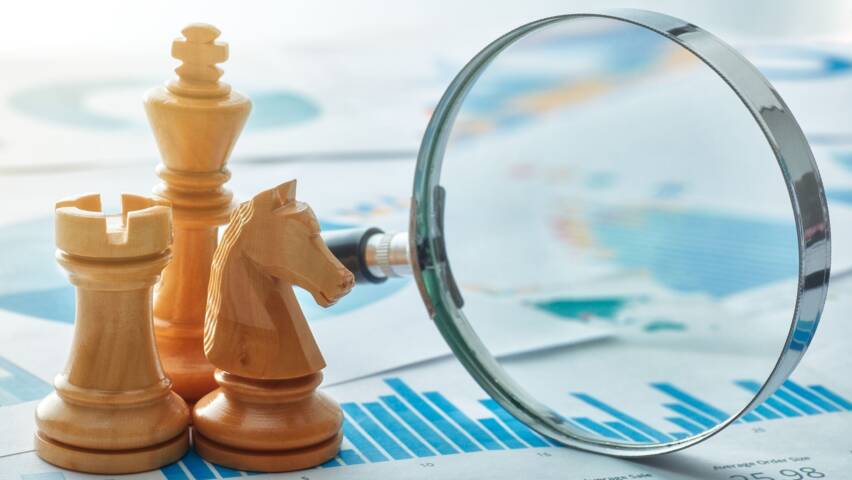 Shakkinappulat ja suurennuslasi kaavioiden päällä symboloivat strategista suunnittelua, analysointia ja tavoitteellista päätöksentekoa.